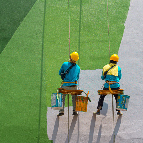 Dois pintores em cadeirinha suspensa pintando uma fachada de verde