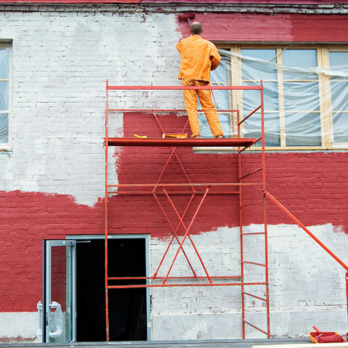 Pintor sobre andaime pintando a fachada de um prédio comercial de vermelho