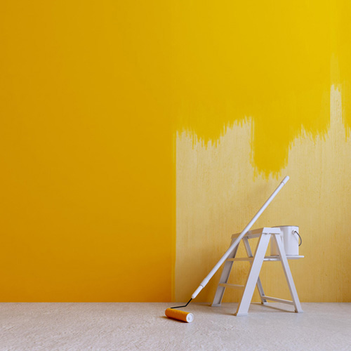 Parede interna sendo pintada de amarelo com rolo e escada